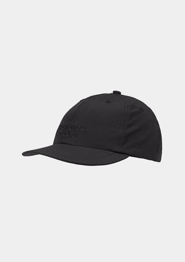 Side view of the Pas Normal Studios Balance Cap in the color Black. Six panel construction and ultra light nylon fabric. Featuring a vented opening on the back and completed with a toggled drawstring, the cap is highly breathable and close-fitting, making it nearly undetectable during use.