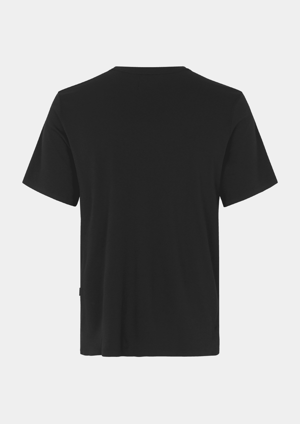 Back view of the Pas Normal Studios Men’s Balance Short Sleeve Top in the color black. Knit construction and split hem vents. No logos are on the back of this shirt. 