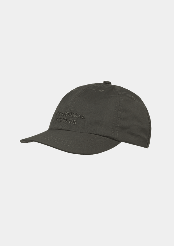 Side view of the Pas Normal Studios Balance Cap in the color dark olive green. Six panel construction and ultra light nylon fabric. Featuring a vented opening on the back and completed with a toggled drawstring, the cap is highly breathable and close-fitting, making it nearly undetectable during use.