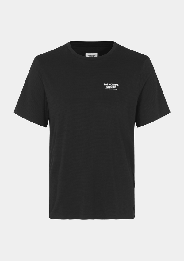 Front view of the Pas Normal Studios Men’s Balance Short Sleeve Top in the color black. Knit construction and split hem vents. Pas Normal Studios text logo in white on front left breast of shirt. 