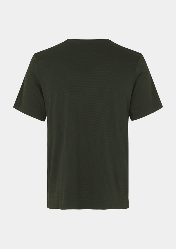 Back view of the Pas Normal Studios Men’s Balance Short Sleeve Top in the color dark olive green. Knit construction and split hem vents. No logos are on the back of this shirt. 