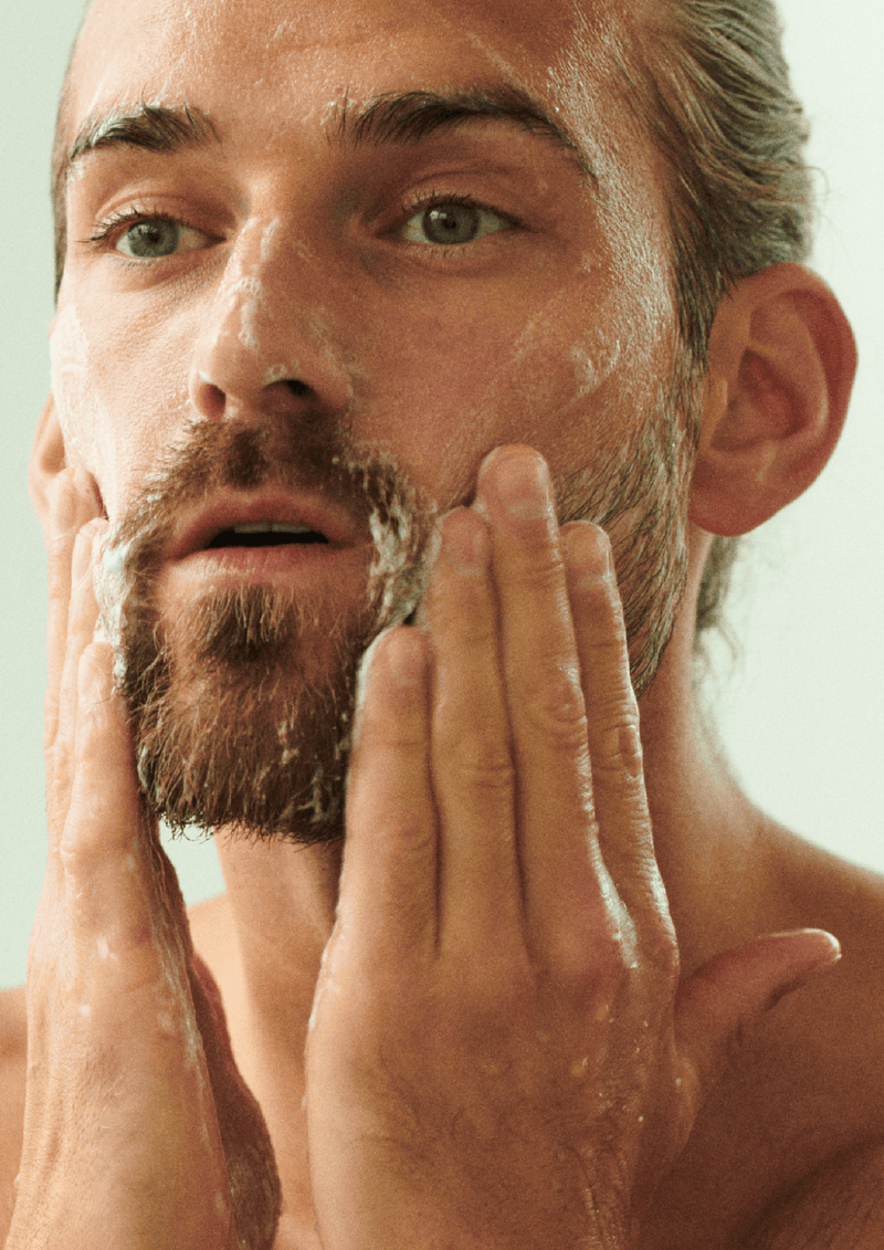 Photo of a man applying the asystem twice daily invigorating cleanser with fingers to his wet face. 
