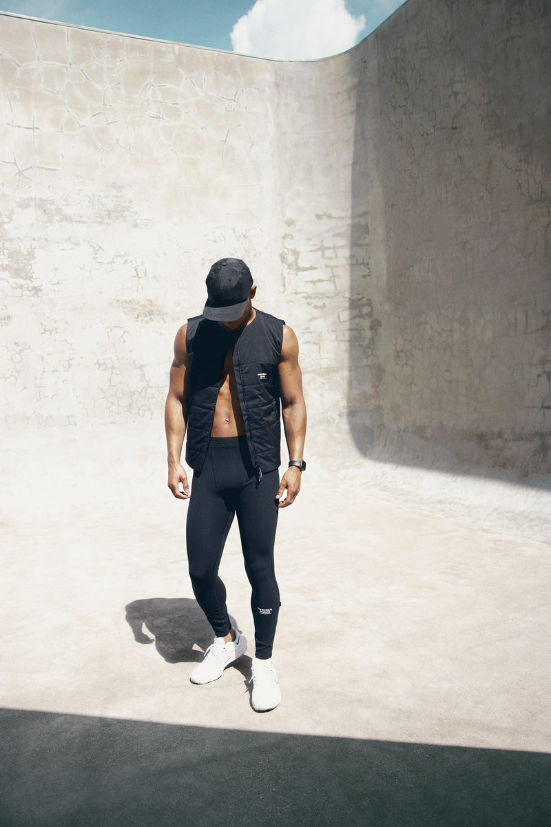 Pas Normal Studios Balance Cap in the color Black. Styled on a man in workout tights and a vest.