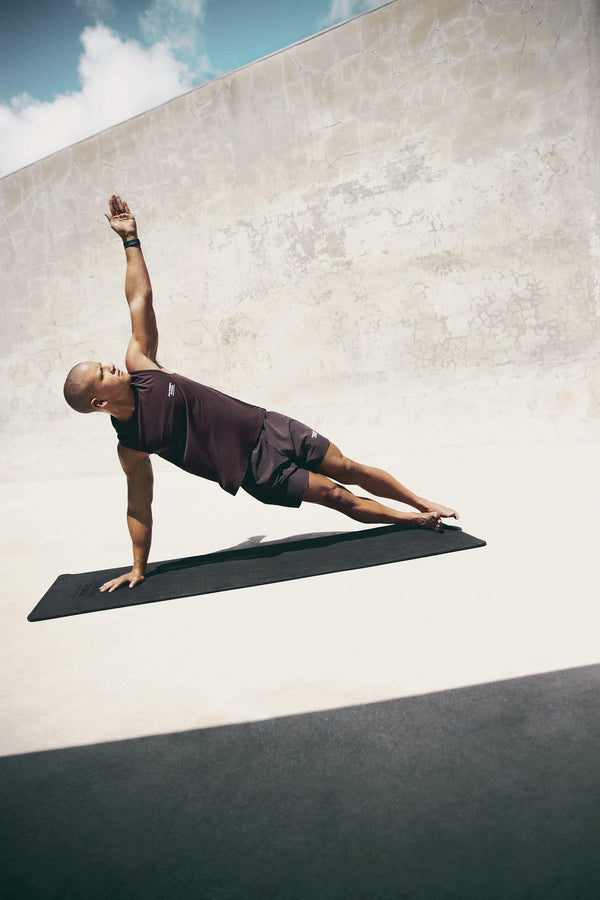 Pas Normal Studios Men’s Balance Sleeveless Top in the color dark red- styled on a man doing yoga
