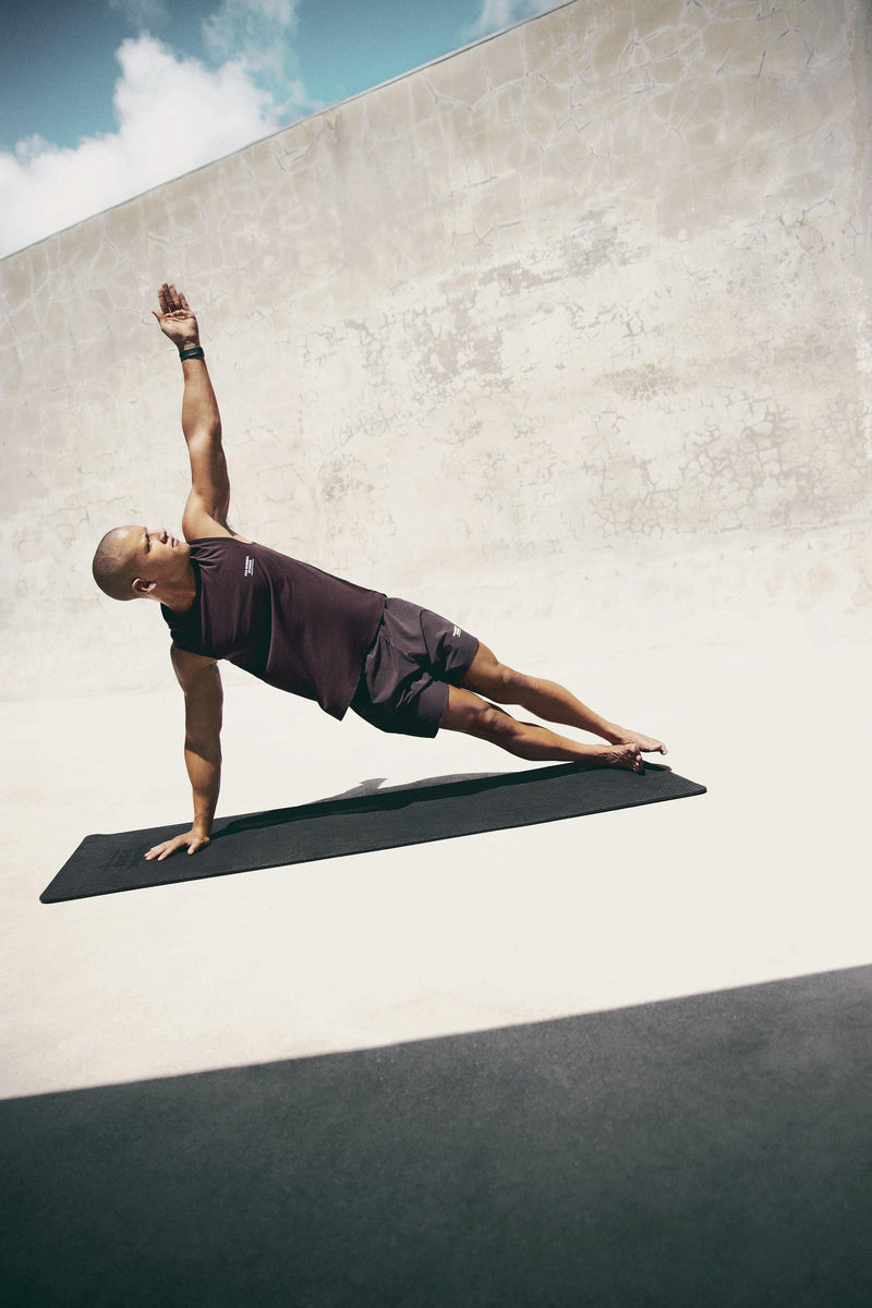 Pas Normal Studios Men’s Balance Sleeveless Top in the color dark red- styled on a man doing yoga