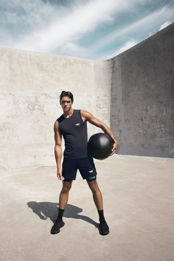 as Normal Studios Men’s Balance Sleeveless Top in the color black. Styled on a man working out with a weighted ball.